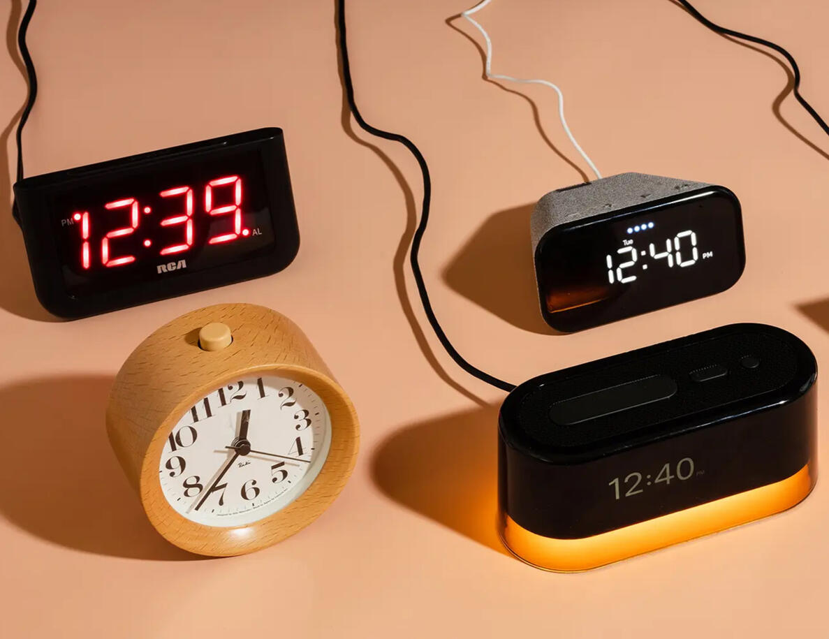 Four alarm clocks on a tan background surface, one is analog and the other three are digital